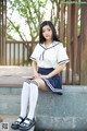 A woman in a school uniform sitting on a bench.