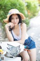 A woman sitting on a motorcycle wearing a straw hat.