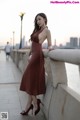 A woman in a brown dress leaning against a wall.