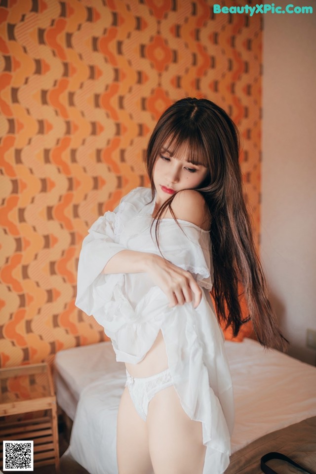 A woman in a white shirt is posing on a bed.