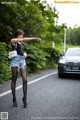 A woman standing on the side of a road next to a car.