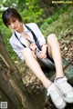 A woman sitting on a bench in the woods holding a knife.