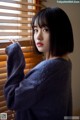 A woman standing in front of a window with blinds.